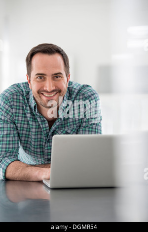Büroeinrichtung. Ein Mann sitzt an einem Tisch mit einem Laptopcomputer. Stockfoto