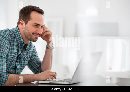 Büroeinrichtung. Ein Mann sitzt an einem Tisch mit einem Laptopcomputer. Stockfoto