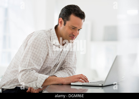 Büroeinrichtung. Ein Mann sitzt an einem Tisch mit einem Laptopcomputer. Stockfoto