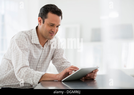 Büroeinrichtung. Ein Mann sitzt an einem Tisch mit einem digitalen Tablet. Stockfoto