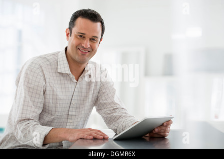 Büroeinrichtung. Ein Mann sitzt an einem Tisch mit einem digitalen Tablet. Stockfoto