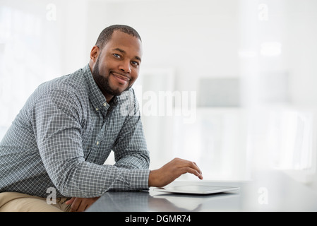 Büroeinrichtung. Ein Mann sitzt an einem Tisch mit einem digitalen Tablet. Stockfoto