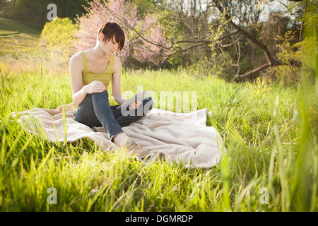 Eine junge Frau sitzt in einem Feld auf einer Decke von einem digitalen Tablet lesen. Stockfoto