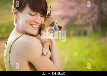 Eine junge Frau auf einer Wiese im Frühjahr. Einen kleinen Chihuahua Hund hält in ihren Armen. Ein Haustier. Stockfoto