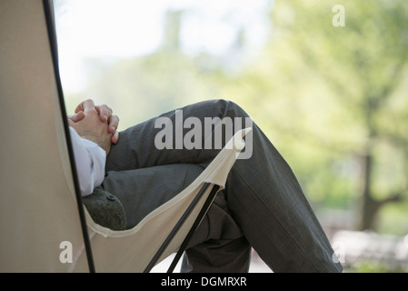 Leben in der Stadt. Ein Mann sitzt in einer Leinwand Campingstuhl im Park. Stockfoto