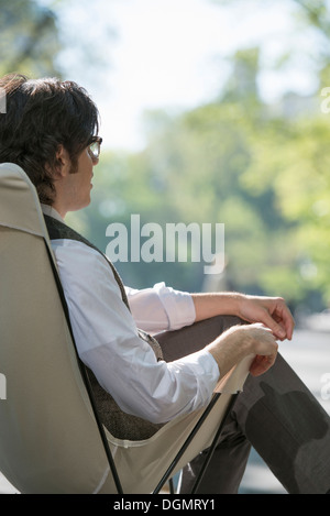 Leben in der Stadt. Ein Mann sitzt in einer Leinwand Campingstuhl im Park. Stockfoto