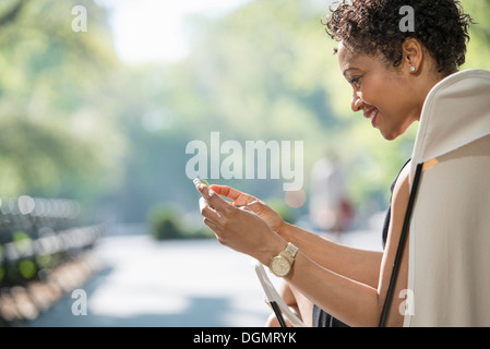 Leben in der Stadt. Eine Frau sitzt auf einem camping Stuhl in einem Stadtpark, überprüft ihr Handy. Stockfoto