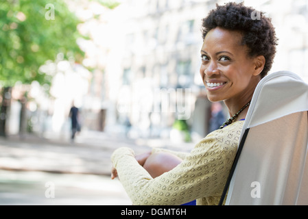 Leben in der Stadt. Eine Frau sitzt auf einem camping Stuhl in einem Stadtpark, über die Schulter schauen. Stockfoto