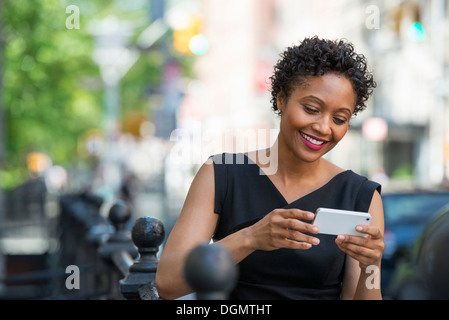 Menschen in Bewegung. Eine Frau in einem schwarzen Kleid auf einer Stadtstraße, überprüft ihr Telefon. Stockfoto