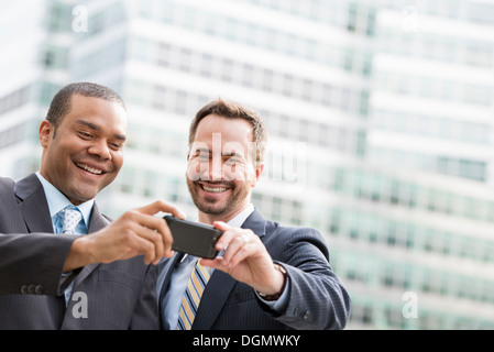 Stadt. Zwei Männer in Anzügen, Blick auf ein smart Phone, lächelnd.