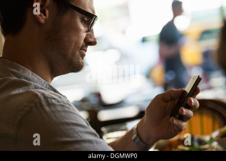 Geschäft unterwegs. Ein Mann sitzt in einem Cafétisch, mit seinem Handy. Blick nach unten auf dem Bildschirm. Stockfoto