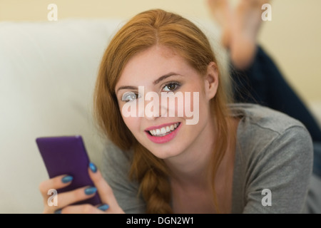 Hübsche Rothaarige lag auf dem Sofa einen Text in die Kamera Lächeln senden Stockfoto