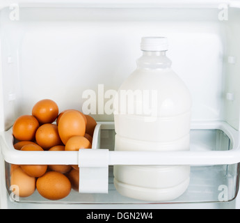 Foto von frischen braunen Bio-Eiern und Milch in Kühlschrank Tür Regal Stockfoto