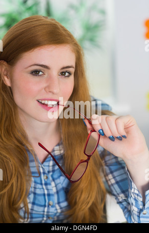 Lächelnde Rothaarige beißen ihre Lesebrille Stockfoto