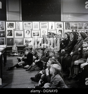 Historisches Bild der 1950er-Jahre, das eine Gruppe von Eltern und Schulkindern zeigt, die in einer Schulhalle bei einer Fotoausstellung in England, Großbritannien, sitzen. Stockfoto