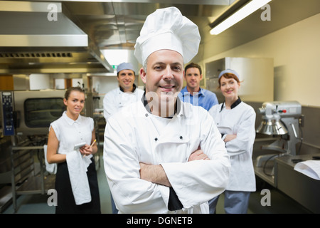 Chefkoch posiert mit Team hinter ihm Stockfoto