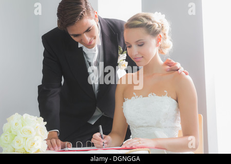 Junge blonde Braut sitzt am Tisch, die Unterzeichnung Hochzeit register Stockfoto