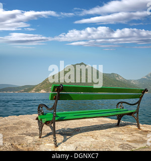 Grüne Holzbank steht im sonnigen Sommermorgen an der Küste der Stadt Perast, Montenegro Stockfoto