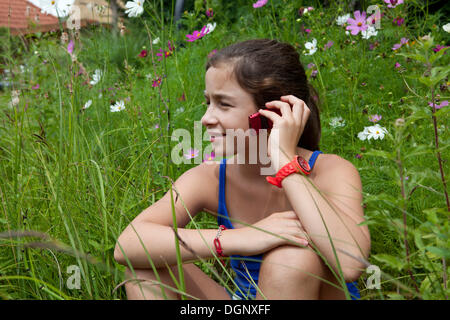 Mädchen, 11 Jahre, sitzt in einer Blumenwiese telefonieren mit einem Handy Stockfoto