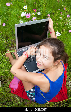 Mädchen, 11 Jahre, sitzt auf einer Wiese mit einem Laptopcomputer Stockfoto