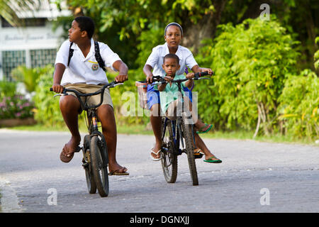 Kinder tragen Schuluniformen beim Radfahren, La Digue Island, Seychellen, Afrika, Indischer Ozean Stockfoto