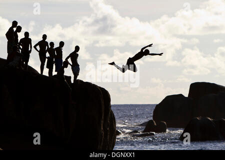 Kreolische Jugendliche springen von Felsen, Silhouetten, Mahé, Seychellen, Afrika, Indischer Ozean Stockfoto