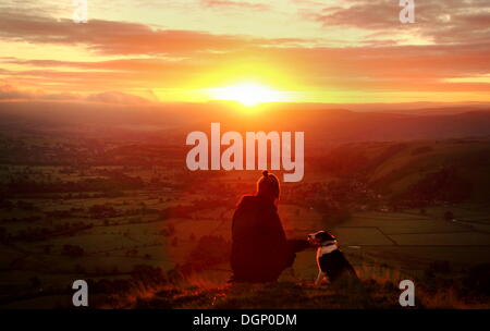 Wanderer mit Hund Zeugen Sonnenaufgang über Hope Valley von Mam Tor; ein Wahrzeichen Hügel in der Nähe von Castleton im Peak District National Park, Derbyshire England UK Stockfoto