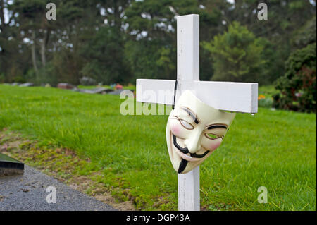 Anonymen Maske, Guy Fawkes Maske hängt ein Kreuz auf einem Friedhof, symbolisches Bild Stockfoto