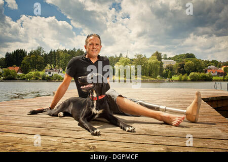 Mann mit einer Beinprothese sitzen auf einem Steg mit seinem Jagdhund Stockfoto