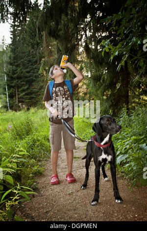 Junge aus einer Flasche trinken zu Fuß seinen Jagdhund Stockfoto