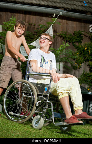 Teenager in einem Rollstuhl sitzt ein Junge hinter ihm steht Stockfoto