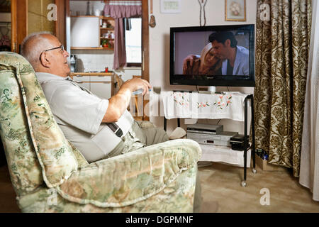 Älterer Mann sitzt vor dem Fernseher eine Fernbedienung in Betrieb Stockfoto