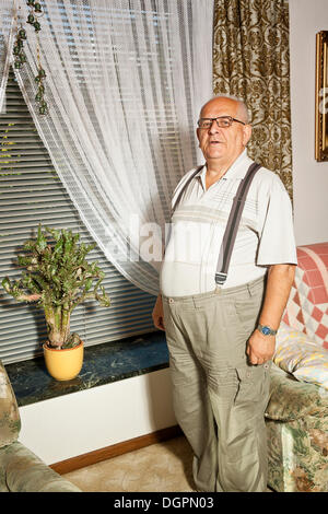 Pensionierter Mann stand vor einem Kaktus auf dem Fensterbrett Stockfoto