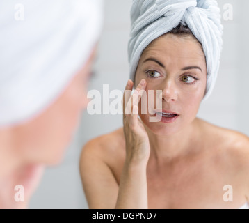 Porträt einer schönen Reife Dame mit einem Handtuch auf dem Kopf, die ihre Haut im Spiegel zu betrachten Stockfoto