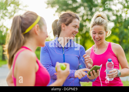 Gruppe von glücklich aktive Mädchen, die Vorbereitung für einen Lauf in Natur durch die Wahl der Musik auf einem Smartphone Stockfoto