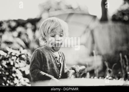 Kleiner Junge mit seinem Mund verschmiert mit Schokolade schockiert mit Blick auf eine Schubkarre Stockfoto