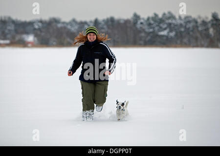 Frau mit einem kleinen Hund durch tiefen Schnee laufen Stockfoto