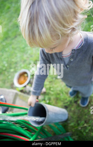 Ein kleiner Junge, stehend auf einem Gartenschlauch Wasser durch ein Rohr zu übergeben Stockfoto