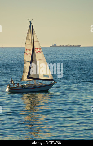 Segelboot auf einem ruhigen Pazifik Abend mit einem super Tanker am Horizont, Redondo Beach, Los Angeles, Kalifornien. Stockfoto