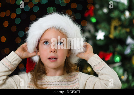 Kleines Mädchen in Nikolausmütze über Weihnachtsbaum Stockfoto