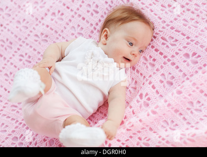 Das Baby liegt auf einem rosa Handtuch. Sie ist in rosa Shorts und eine weiße Bluse. Stockfoto