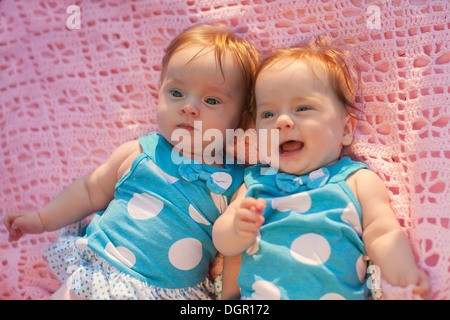 Süße kleine Zwillinge liegen auf einer rosa Decke. Sie im blauen Kleid mit weißen Tupfen. Stockfoto