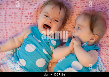 Süße kleine Zwillinge liegen auf einer rosa Decke. Sie im blauen Kleid mit weißen Tupfen. Stockfoto