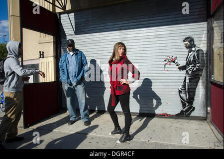 Street-Art-Fans strömen in Flynts Hustler Club im Stadtteil "Hells Kitchen" von New York auf Donnerstag, 24. Oktober 2013, "Waiting in vain" der vierundzwanzigste Ausgabe von Banksy-Graffiti-Kunst zu sehen. Die Schablone Darstellung ist auf das Rollup-Tor am Eingang der Gentlemen Club, das Sicherheitspersonal außerhalb entsandt hat, um ihr neues Meisterwerk zu schützen.  Die schwer fassbare Streetart-Künstler schafft Werke rund um die Stadt jeden Tag im Laufe des Monats Oktober "Besser aus als In" genannt.  (© Frances M. Roberts) Stockfoto