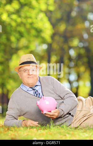 Zufrieden ältere Gentleman in einem Park hält ein Sparschwein Stockfoto