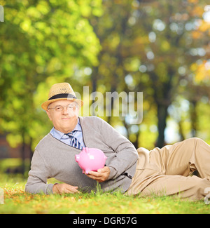 Zufrieden ältere Gentleman in einem Park hält ein Sparschwein, Stockfoto