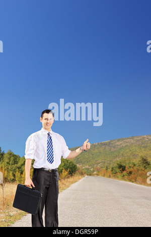 Junge Unternehmer halten einen Koffer und per Anhalter auf einer Straße Stockfoto