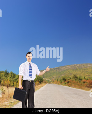 Junge Unternehmer halten einen Leder-Koffer und per Anhalter auf einer offenen Straße Stockfoto