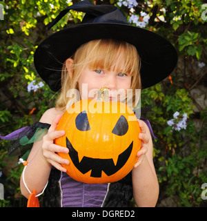 Blonde kurzhaarige Mädchen verkleidet in einem Hexen-Outfit hält einen Kürbis für Halloween. Stockfoto