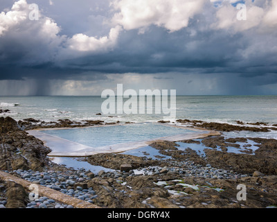 Der Rock Pool Swimmingpool im Westward Ho! Und ein Sommerregensturm über dem Atlantik in der Ferne an der Küste von North Devon, England. Stockfoto